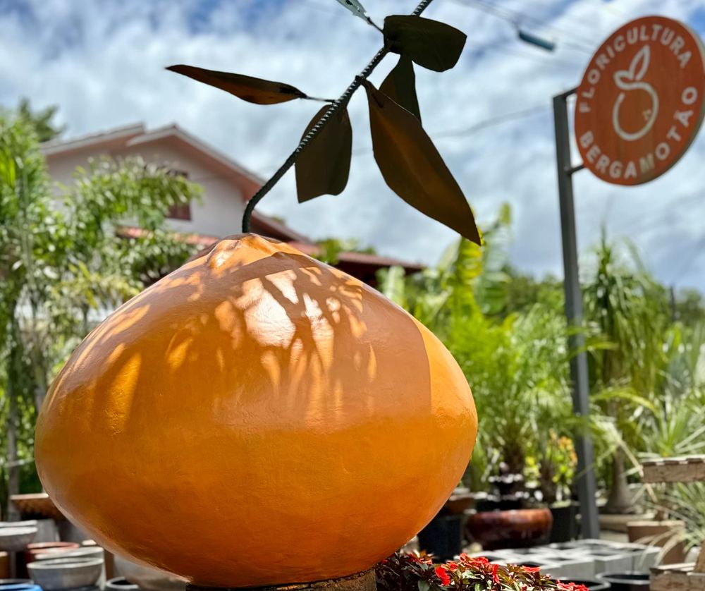 Escultura de bergamota laranja e placa da Floricultura Bergamotão junto ao canteiro da loja.