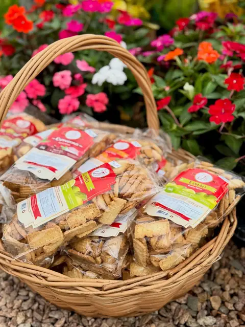 Cesto de vime com pacotes de biscoito, flores ao fundo