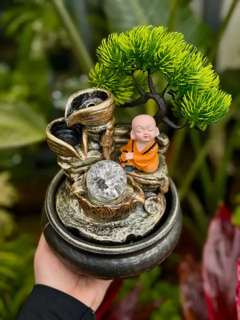 Fonte com monge de laranja e bonsai artificial, na mão