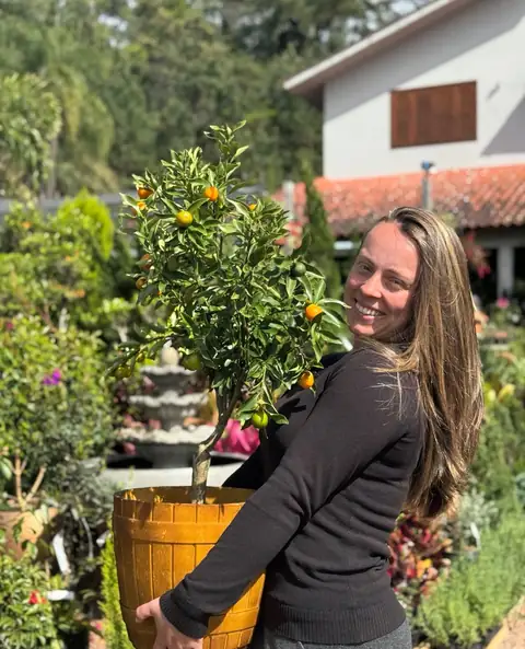 Kinkan com frutos laranja em vaso de madeira, dona sorrindo