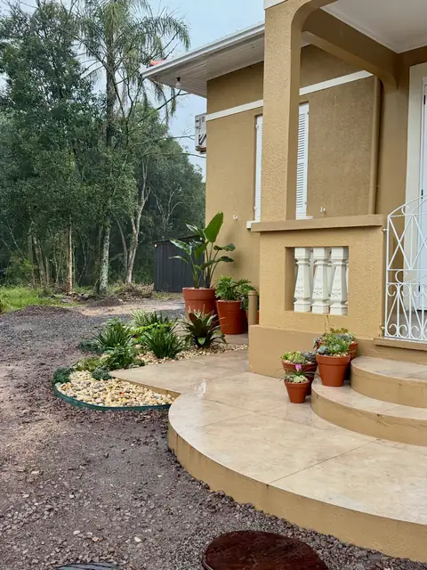 Casa amarela com canteiro de seixos e vasos de barro