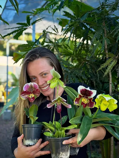 Dona sorrindo com orquídeas sapatinho em vasos